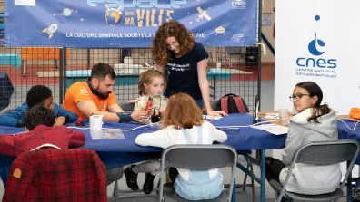 Deux intervenants, un homme assis et une femme debout, avec des enfants assis autour d'une table