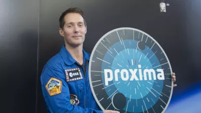 Photographie de Thomas Pesquet posant avec le logo de la mission Proxima